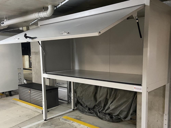 Large over bonnet storage locker with lift-up lid in parking garage.