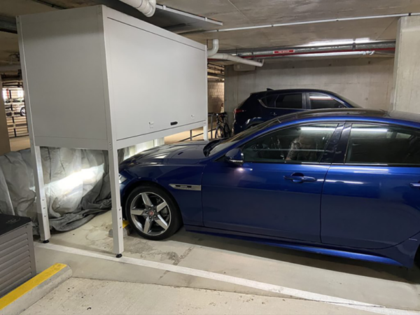Large storage locker installed over a blue car in underground parking.
