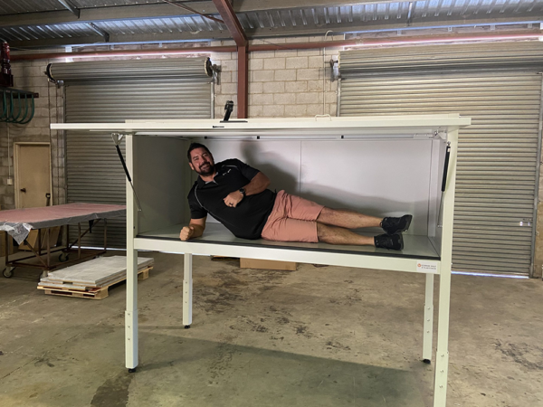 Man lying inside a small over bonnet storage cabinet in workshop setting.